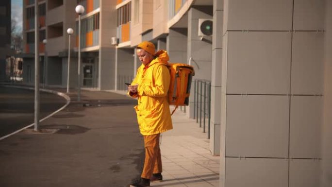 穿着黄色衣服的男子快递员运送食物-拿着电话走出门廊