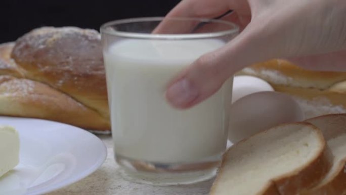 女性手拿一杯牛奶，背景是烘焙产品、黄油、鸡蛋。早餐。乳制品。
