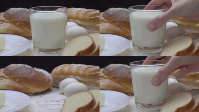 女性手拿一杯牛奶，背景是烘焙产品、黄油、鸡蛋。早餐。乳制品。