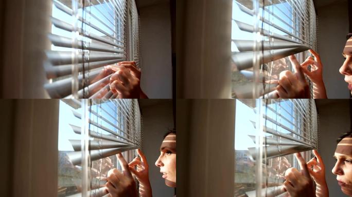 室内特写肖像，迷人的黑发女人用手推着窗户的百叶窗。害怕向外看，因为害怕细菌。检疫的概念，自我隔离