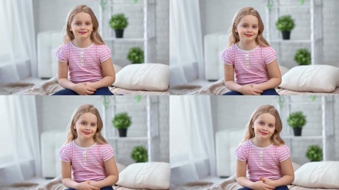 肖像可爱的金发小女孩微笑着坐在舒适的家里的床上。4k龙红相机