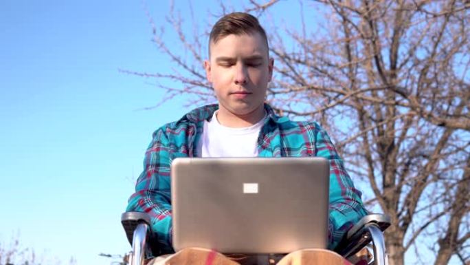 坐在轮椅上的年轻人带着笔记本电脑。自然界中的残疾人在笔记本电脑上进行远程工作。