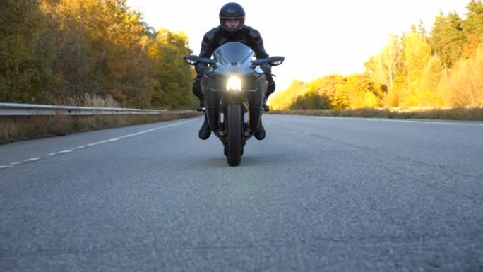 摩托车手在乡间小路上骑摩托车。戴着头盔的年轻人在高速公路上快速骑现代运动摩托车。旅途中开车的人。冒险