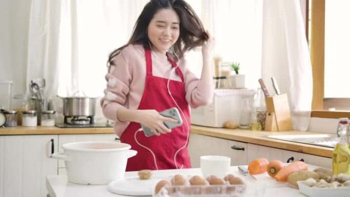 年轻的亚洲妇女用手机听音乐，在厨房跳舞。