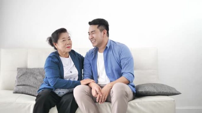亚洲母亲抱着儿子坐在家里的沙发上，生活方式观念。