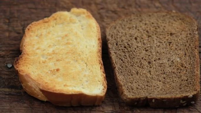 在一块木制棕色板上放两片烤黑麦和白小麦粉面包