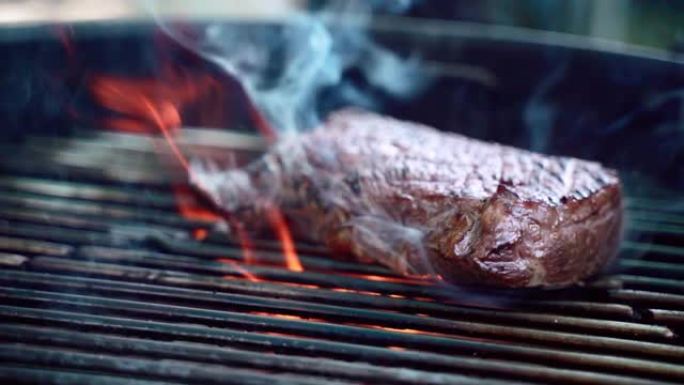 美味多汁的牛肉牛排在火盆的烧烤网格上烤烟和燃烧的火焰，户外慢动作烧烤。在炭火上用香料和香草烤和油炸生