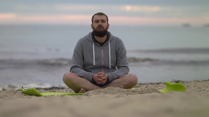留着胡须的男人坐在海滩上，四处张望-4k拍摄。