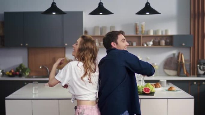 幸福的夫妇在家庭厨房背靠背跳舞。兴奋的朋友玩得开心。