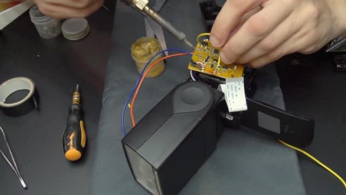 车间的一位大师修理相机闪光灯，焊接和检查电子元件。