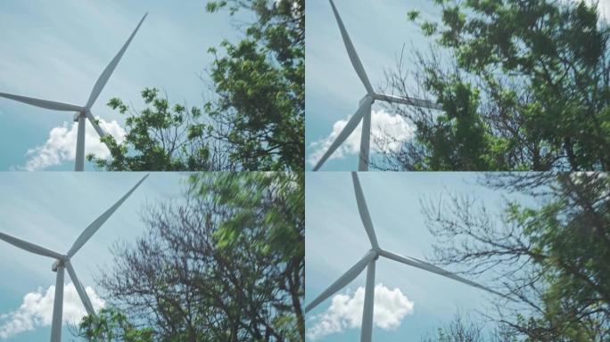 风力涡轮机的移动镜头，视图来自带有汽车的移动车辆。明亮的蓝天，有干净的白云，拍摄于夏日。绿色能源