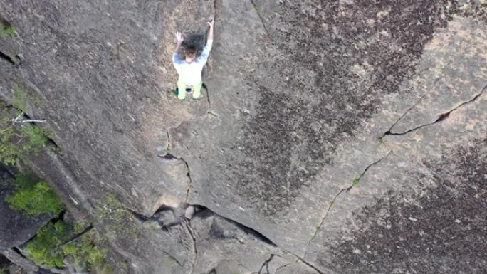 一个勇敢的人在没有保险的情况下爬到岩壁上的山顶的俯视图。
