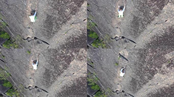 一个勇敢的人在没有保险的情况下爬到岩壁上的山顶的俯视图。