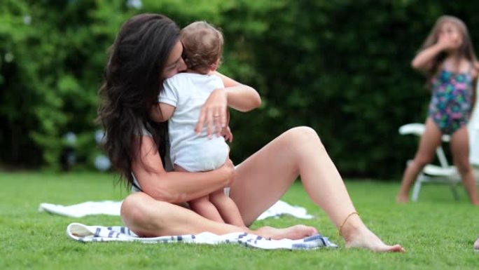 坦率的母亲在草坪上照顾和拥抱婴儿