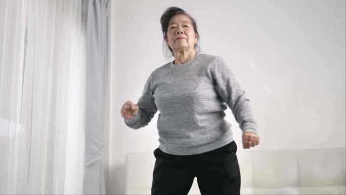 亚洲老年妇女在家里锻炼和跳舞，呆在家里的生活方式概念。缓慢的运动。