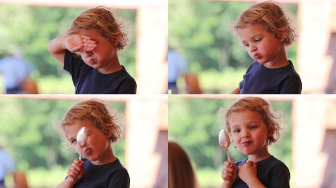 金发小男孩躲在镜头前，手和勺子可爱可爱