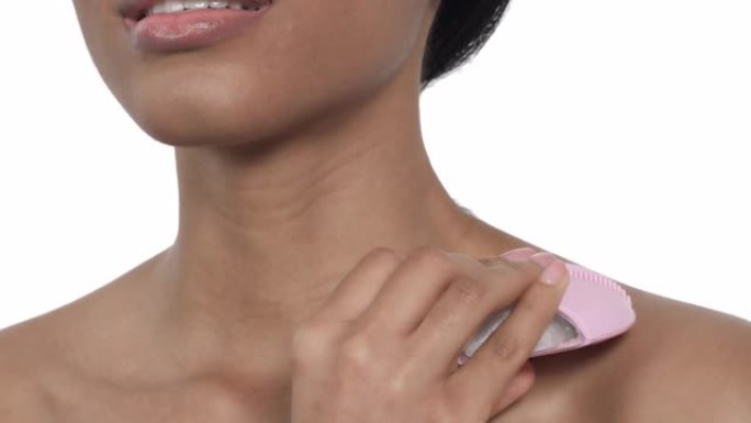 一个女人在脖子上使用化妆品清洁按摩刷的特写镜头。护肤，抗衰老理念。孤立，在白色背景上