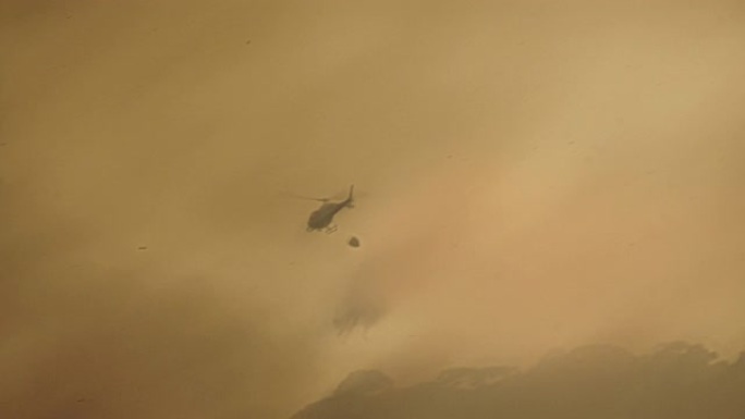 消防员直升机在森林大火中从水桶中滴水