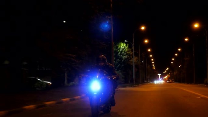 男子骑在现代运动摩托车上，晚上开着前灯。摩托车手在昏暗的城市街道上骑摩托车。旅途中开车的人。自由和冒
