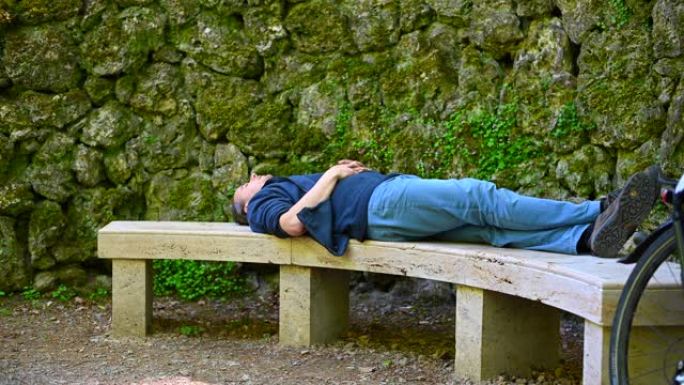 一个人躺在石凳上，背景是旧石墙，放松身心