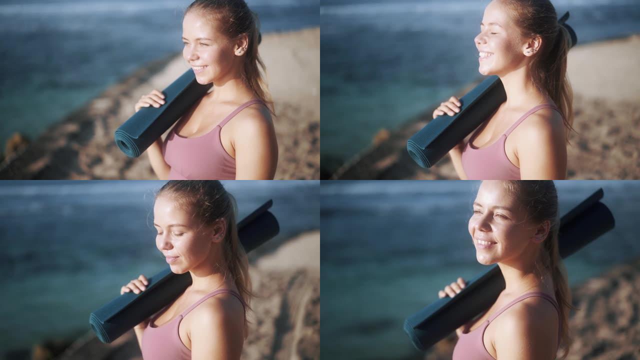 马尾辫快乐的好女孩在海滩上拿着瑜伽垫
