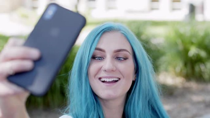 独特的时髦年轻女子，有趣可爱的蓝绿色染发，使用她的移动手机智能手机作为有影响力的人自拍或视频博客，并