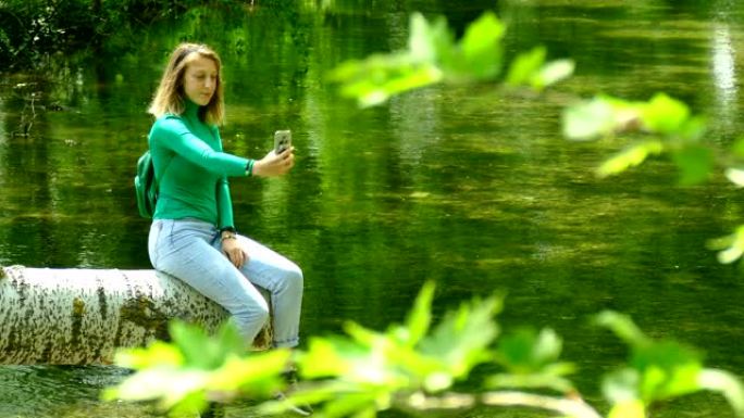 年轻女子在森林河上用智能手机休息