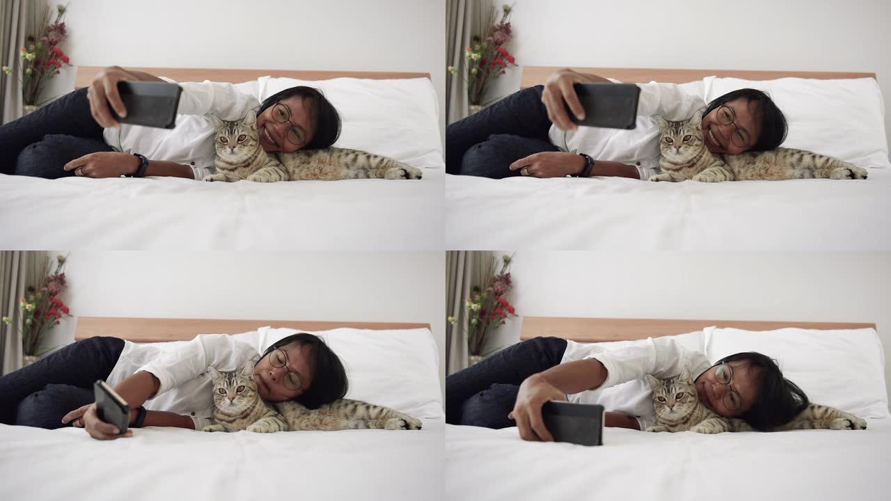 亚洲女性使用智能手机自拍，在现代卧室玩虎斑猫。