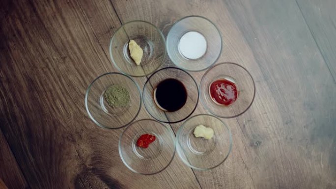 各种类型的香料在玻璃碗上的木制棕色桌子: 盐，大豆酱，番茄酱，姜酱，大蒜酱，辣椒酱，黑胡椒粉。旋转摄