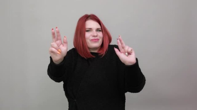 穿着黑色毛衣的年轻红发胖女人快乐的女人展示双手上的两个手指