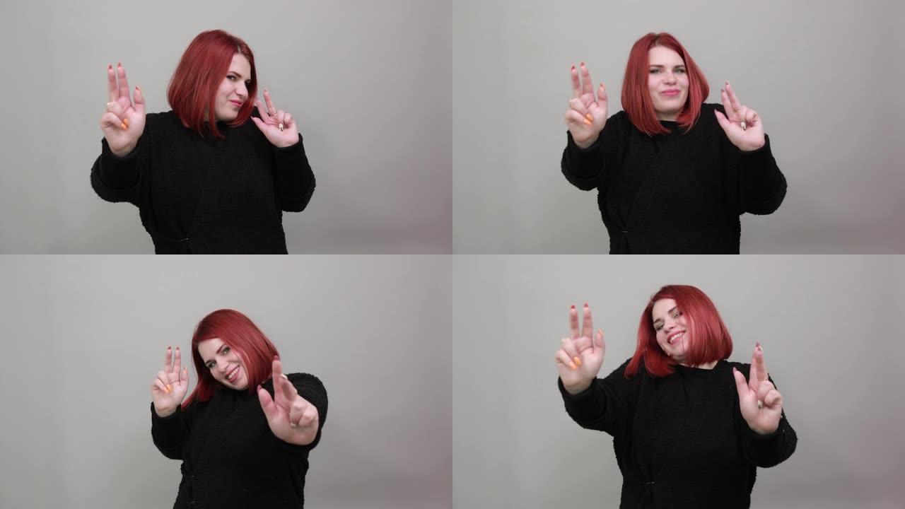 穿着黑色毛衣的年轻红发胖女人快乐的女人展示双手上的两个手指