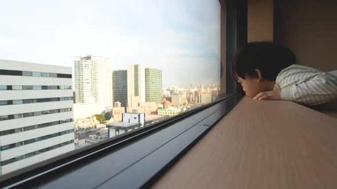 亚洲小孩看着窗外的全景城市建筑。