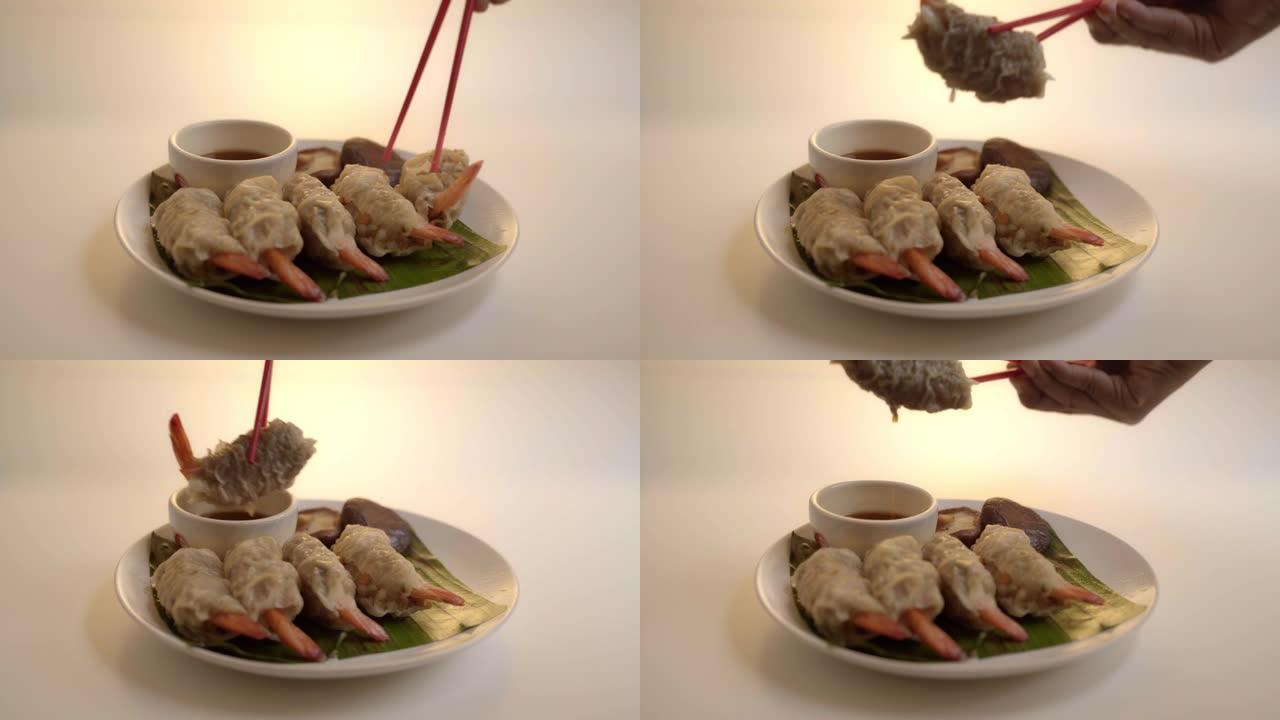 特写筷子采摘亚洲蒸汽饺子或点心一种著名的中国菜，香蕉叶上有猪肉和虾，白色桌子上有白菜。