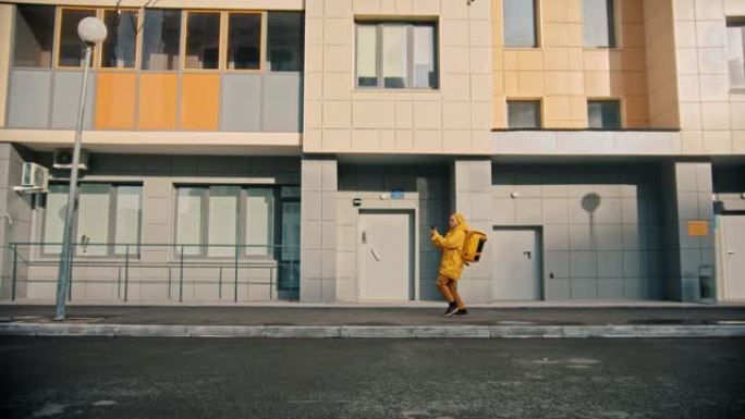 穿着黄色衣服的男子快递员送食物-在房子附近跑，急忙-看着电话