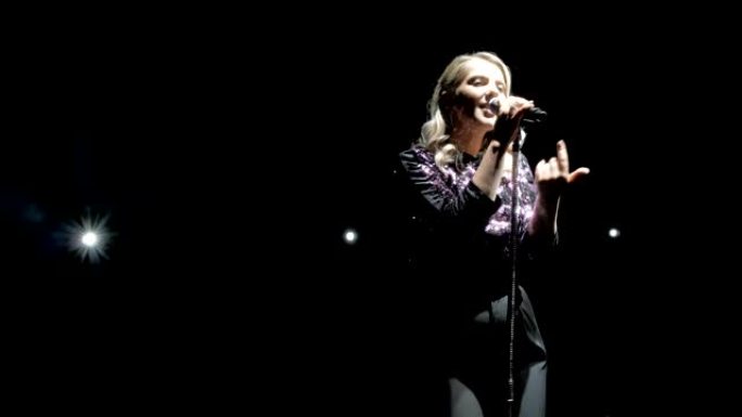 舞台上的女歌手。歌手在明亮的灯光背景下向麦克风唱歌。