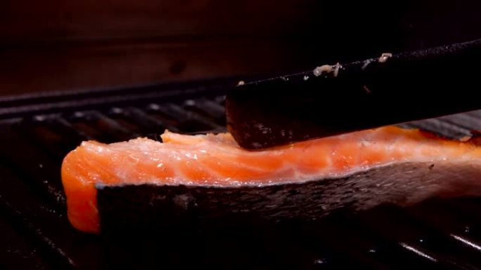 库克在烤架上用黑色抹刀翻转一块鲑鱼片