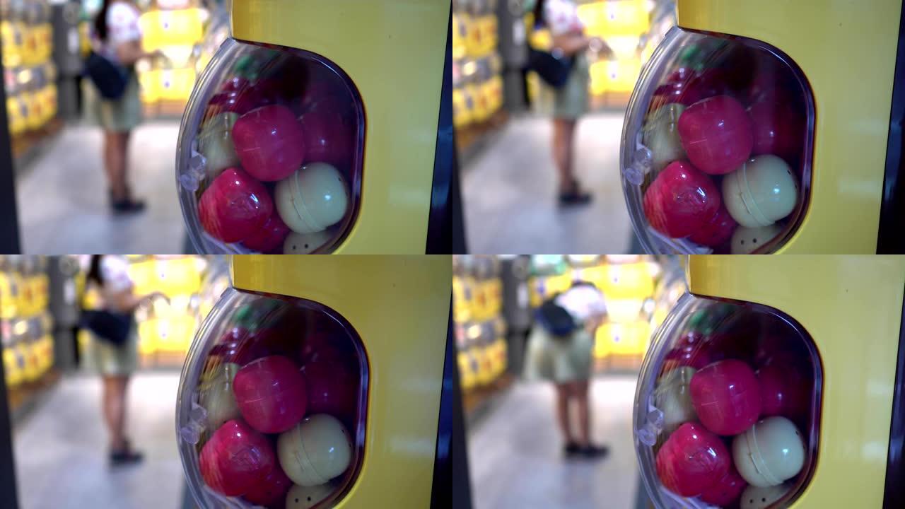 胶囊玩具机的特写镜头。背景模糊是一个站在玩具前的小女孩。