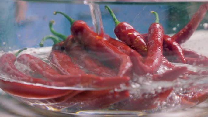 用清水倒入新鲜的红辣椒，用玻璃花瓶清洗清洗。素食主义者的健康营养食品。广告/电影4K的美丽镜头