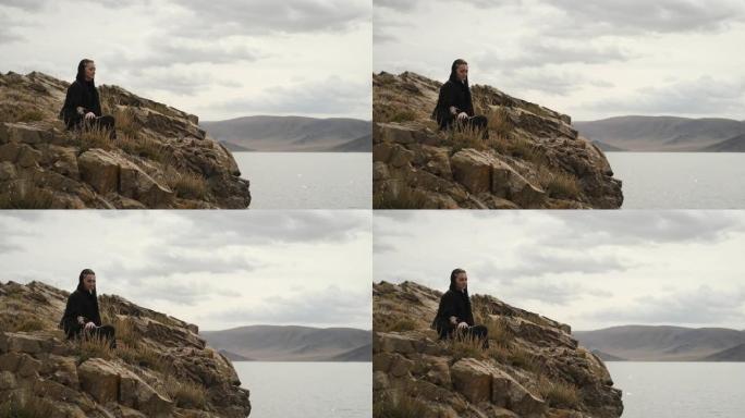 穿着黑色连衣裙的女人坐在山顶的悬崖边。大湖