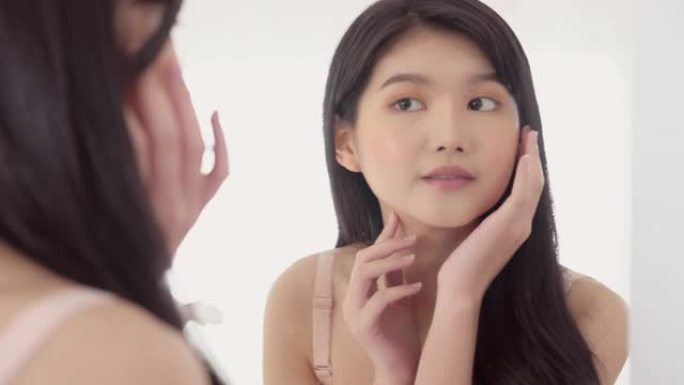 美丽的年轻亚洲女人微笑着看着镜子，用皮肤护理和化妆品来恢复活力和卫生，美容女孩用面霜或乳液和健康快乐