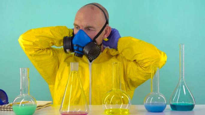 一名化学实验室的员工穿着黄色防护服，戴着手套和口罩，完成了实验，脱下了防护服，窒息而死，摔倒在桌子上