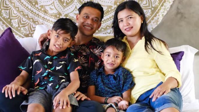 东南亚家庭在家里度过时光。快乐的印度尼西亚或马拉西亚父母和孩子躺在床上一起玩得开心