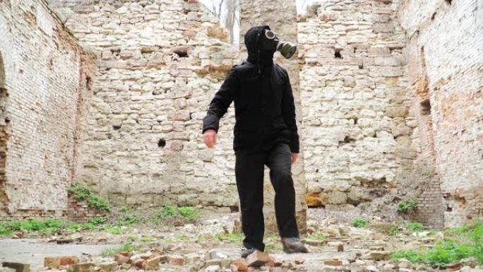戴着防毒面具和黑色衣服的人是这座废弃建筑的废墟之一。跟踪者概念，核化学战争后的幸存者。慢动作。在St