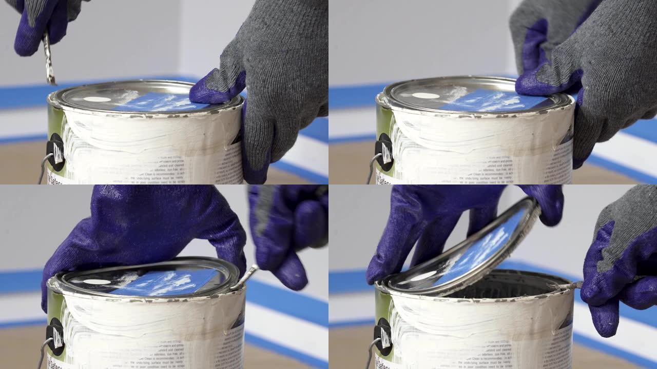 4k，戴着手套的手在开始油漆室之前用开罐器打开一罐白色油漆。
