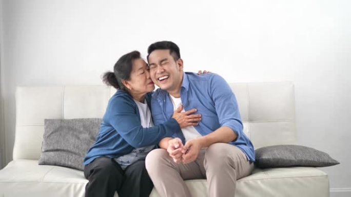 亚洲母亲抱着儿子坐在家里的沙发上，生活方式观念。