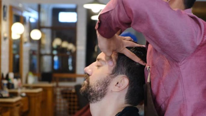 年轻男子理发后在理发店或发廊做头部按摩。理发店客户按摩主管