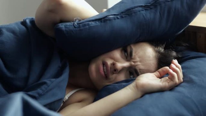 年轻女子在检疫期间呆在家里。不快乐的不愉快女孩躺在床上，遮住脸，免受噪音或晨光。该醒来了。