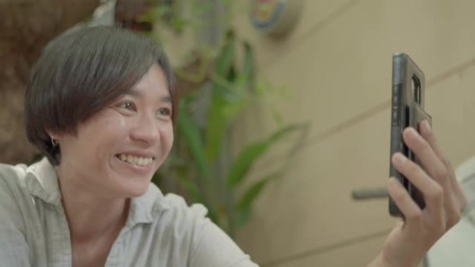 微笑的亚洲女人在家通过智能手机聊天。