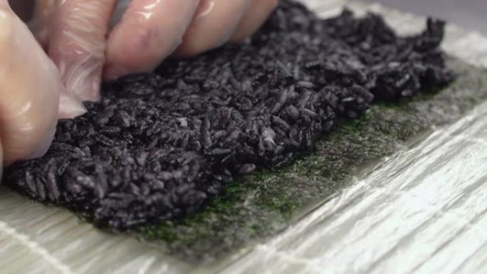 厨师将黑米放在紫菜上，使寿司慢动作滚动