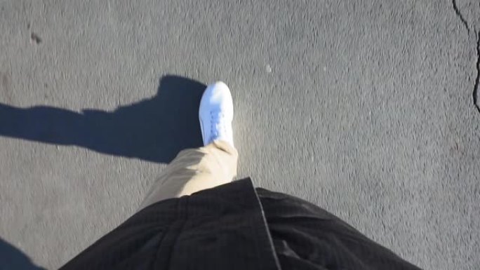 在阳光明媚的日子里，穿着白色运动鞋的男人穿着牛仔裤走在人行道上。视点视频，第一人称